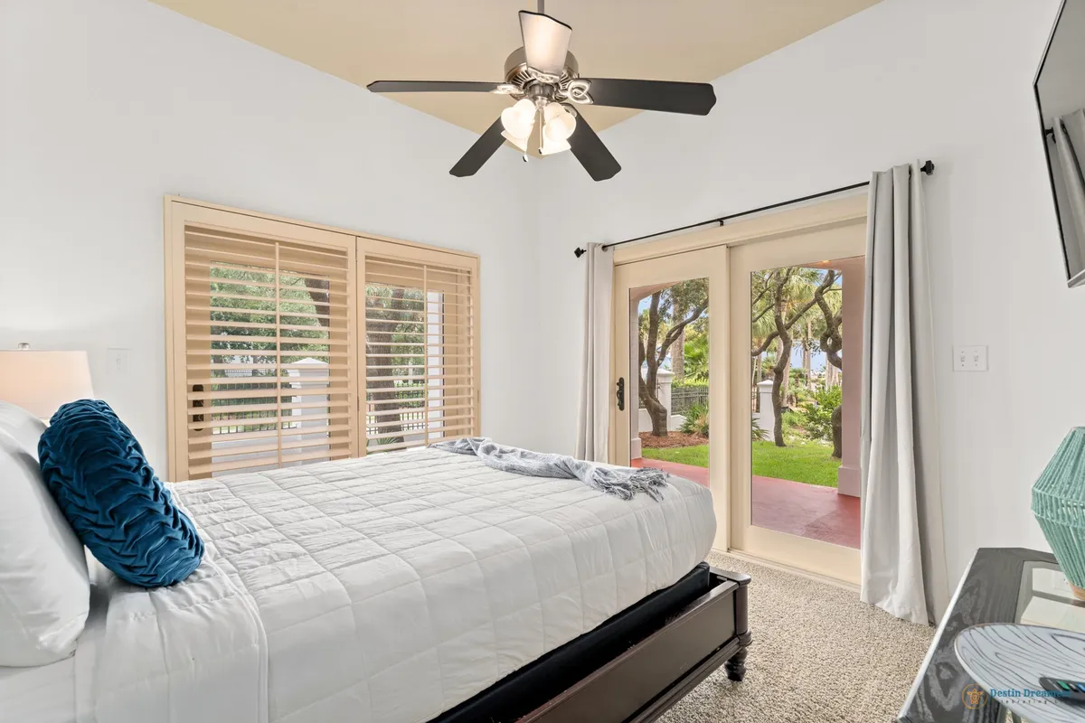 A peaceful bedroom scene featuring a large bed with white bedding and a blue accent pillow, flanked by sliding glass doors that open onto a garden view. Natural light floods the room, highlighting the seamless access to the outdoors and the tranquil setting ideal for relaxing after a day of exploration.
